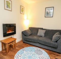 A living room with a gray sofa a round rug and a wall-mounted electric fireplace at Honeysuckle Cottage in Crossgates