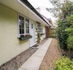 A walkway along a house exterior with flower boxes on windows and a wooden gate at Primrose Cottage in Crossgates