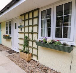 The exterior of a building with windows flower boxes a white door and a sign reading Primrose Cottage at Crossgates
