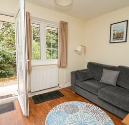 A living room with a gray sofa round patterned rug open door and a window at Primrose Cottage in Crossgates