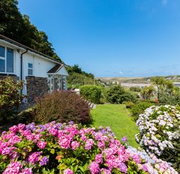 A garden with pink and white flowers next to a house with a view of a coastal town and hills at Beach Haven in Polzeath