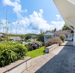 An outdoor patio area with stone tiles and steps leading to a grassy garden with bushes and flowers at Beach Haven in Polzeath