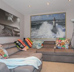 A living room with a gray sectional sofa with colorful cushions and two framed pictures on the walls at Alltwen in Borth-y-Gest