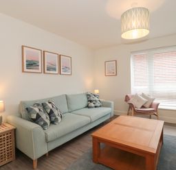 A living room with a sofa, armchair, coffee table, side table with lamp, and framed pictures on walls at Apartment 1 in Exmouth