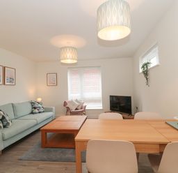 A living room with a sofa a coffee table a dining table chairs a TV and framed pictures at Apartment 1 in Exmouth