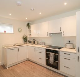 A kitchen with white cabinets microwave kettle oven and wooden floor at Apartment 1 in Exmouth
