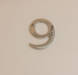 A metallic number 9 mounted on a plain white wall at Apartment 9 in Exmouth