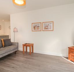 A living room with a gray sofa, wooden side table, floor lamp, two framed pictures on the wall, and a wooden TV stand with a television at Apartment 9 in Exmouth