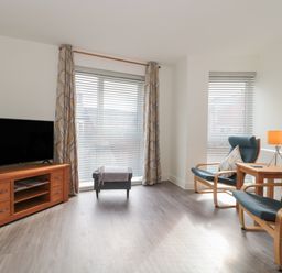 A living room with a television on a wooden stand and two armchairs with cushions at Apartment 9 in Exmouth