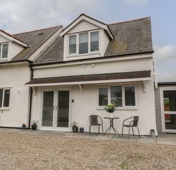 Outside view of a white two-story house with dormer windows and a small patio set with two chairs and a table with flowers at Bryn Eglwys Bach in Penmynydd near Llanfairpwllgwyngyll