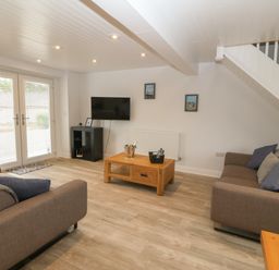 A living room with two sofas a wooden coffee table a TV on a stand and double glass doors at Bryn Eglwys Bach in Penmynydd near Llanfairpwllgwyngyll