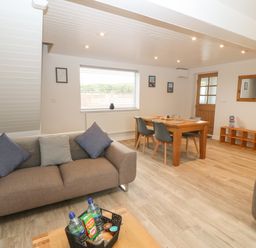 A living room with two sofas a dining table with chairs a window a door and a wooden shelf at Bryn Eglwys Bach in Penmynydd near Llanfairpwllgwyngyll