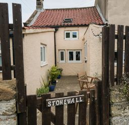 A small courtyard with potted plants and a wooden chair behind a wooden gate with a stone wall at Stonewall Sandsend