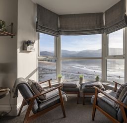 A sitting area with two armchairs facing a large bay window overlooking a beach and mountains at Harbour View Flat 2 in Barmouth