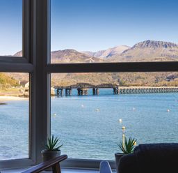 A window view of a body of water with a bridge and mountains in the background at Harbour View - Flat 2 in Barmouth