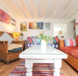 A living room with wicker armchairs sofas and a white coffee table with flowers at Rose Cottage Lower Bostraze near St Just