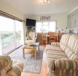 A living room with patterned sofas a wooden coffee table a dining table with chairs and a wall-mounted television at Morlyn Guest House Apartment in Llandanwg near Harlech