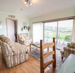 A living room with sofas a coffee table a wall clock and a sliding glass door at Morlyn Guest House Apartment Llandanwg near Harlech