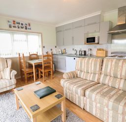 A living room and kitchen area with a sofa armchair wooden dining table and chairs and kitchen cabinets at Morlyn Guest House Apartment in Llandanwg near Harlech