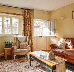 A living room with a striped armchair and brown leather sofa near a half-glazed door at Bodkin Cottage in Dunster