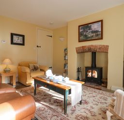 A living room with a wood burning stove coffee table armchairs and a rug at Bodkin Cottage in Dunster