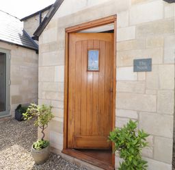 An open wooden front door on a stone building with potted plants and a sign reading The Nook at Jack's Green near Painswick