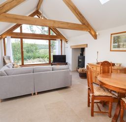 A living room with wooden beams a gray sofa a round wooden dining table and large window at The Nook in Jacks Green near Painswick