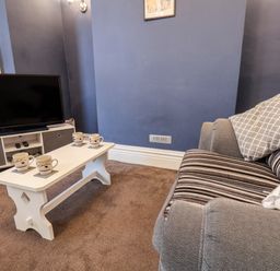 A living room with a striped sofa a white coffee table with four mugs a television and a media unit at 89 Caledonia Street in Scarborough