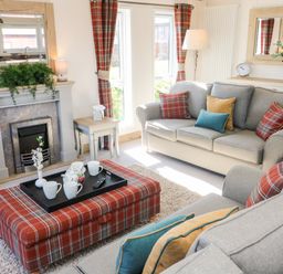 A living room with sofas cushions plaid ottoman and fireplace at Curlew Lodge in Carnforth