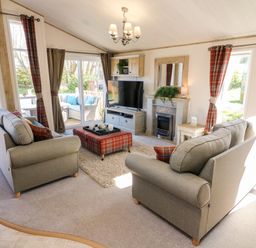 A living room with two sofas a television on a cabinet a fireplace and plaid curtains at Curlew Lodge in Carnforth