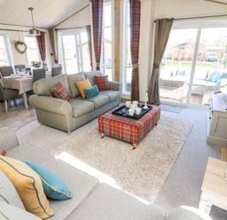 A living room with sofas a plaid ottoman and a dining area in the background at Curlew Lodge Carnforth