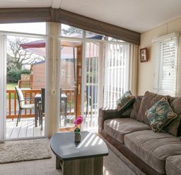 A living room with a sofa a coffee table and glass doors opening to a deck with chairs and an umbrella at Audrey's Lodge Foxburrow Hang in Fritton