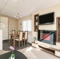 A dining area with a wooden table and chairs and a living space with a wall-mounted television and fireplace at Audrey's Lodge Foxburrow Hang in Fritton