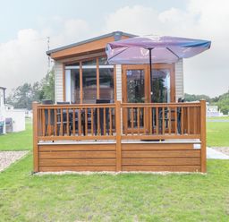 A small wooden deck with chairs and a table under an umbrella outside a cabin at Audreys Lodge Foxburrow Hang in Fritton