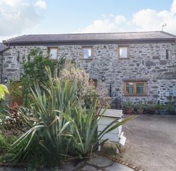 A stone house with multiple windows and a garden with plants and a white beehive in front at Ty Gwennol in Llanddona near Beaumaris