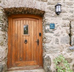 A wooden door set in a stone wall with a small window a door knocker and a wall lamp at Ty Gwennol in Llanddona near Beaumaris