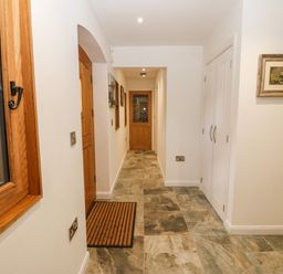 A hallway with stone tile flooring wooden doors a window with wooden frame and white walls at Ty Gwennol in Llanddona near Beaumaris