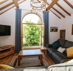 A living room with a large arched window gray sofas and a wooden coffee table at Ty Gwennol in Llanddona near Beaumaris