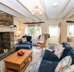 A living room with a stone fireplace wooden coffee table blue furniture and a rocking chair at Alexanders Cottage in Frogmore