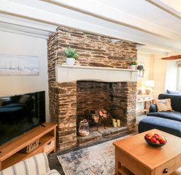 A living room with a stone fireplace a television on a wooden stand and seating at Alexanders Cottage in Frogmore