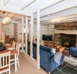 A dining area with a wooden table set for four and a living room with blue couches and a stone fireplace at Alexanders Cottage in Frogmore
