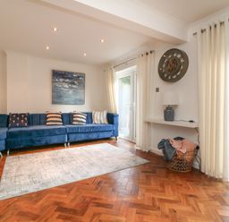 A living room with a blue sectional sofa and pillows a wall clock on the wall and a basket with blankets near glass doors at 4 Woodland Park in Northam
