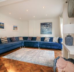 A living room with a blue sectional sofa pillows paintings a table lamp and a rug at 4 Woodland Park in Northam