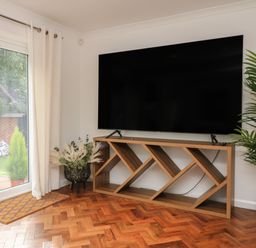 A television on a wooden stand with plants near a glass door in a room at 4 Woodland Park in Northam