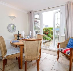 A dining area with a round wooden table and wicker chairs next to open glass doors leading to a garden at Angorfa Bach in Abersoch