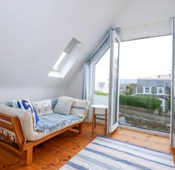 A sitting area with a sofa chair a small round table and an armchair near a large open window at Angorfa Bach in Abersoch