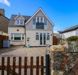A two-story house with a wooden gate driveway and stone wall with flowers at Angorfa Bach in Abersoch