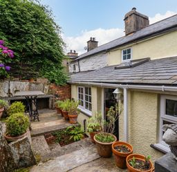 A stone patio with potted plants and a table outside a yellow stone house at Preswylfa in Ffestiniog