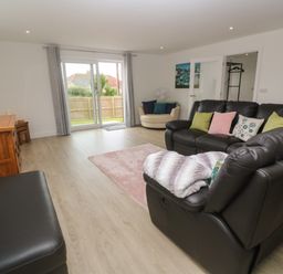 A living room with a black leather sofa, a wooden cabinet, a round beige chair, and sliding glass doors at 3 Praa Cove in Praa Sands