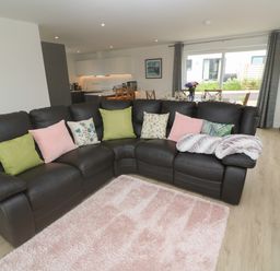 A living room with a brown leather sectional sofa and colorful cushions near a pink rug and a fireplace at 3 Praa Cove in Praa Sands